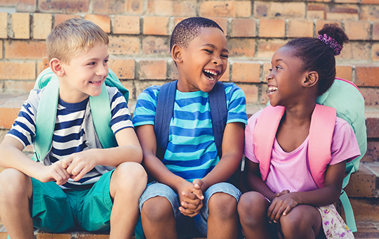 three children with backpacks laughing